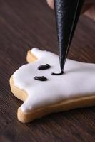 Close up of decorating cute Halloween ghost cookies with frosting. photo