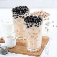 Bubble milk tea with tapioca pearl topping ingredient, famous Taiwanese drink on white wooden table background in drinking glass, close up, copy space photo