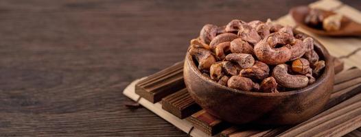 Cashew nuts with peel in a wooden bowl on wooden tray and table background, healthy raw food plate. photo