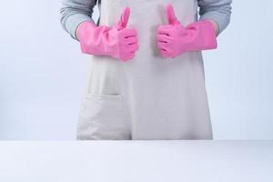 una joven ama de llaves en delantal lleva guantes rosas para limpiar la mesa, concepto de prevención de infecciones por virus, servicio de limpieza, cierre. foto