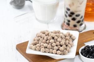 Bubble milk tea with tapioca pearl topping ingredient, famous Taiwanese drink on white wooden table background in drinking glass, close up, copy space photo