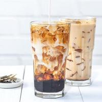 Making bubble tea, pouring blend milk tea into brown sugar pattern drinking glass cup on white wooden table background, close up, copy space photo