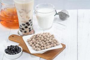 Bubble milk tea with tapioca pearl topping ingredient, famous Taiwanese drink on white wooden table background in drinking glass, close up, copy space photo