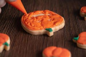 cerca de decorar lindas galletas de calabaza de halloween con glaseado en bolsa de hielo. foto