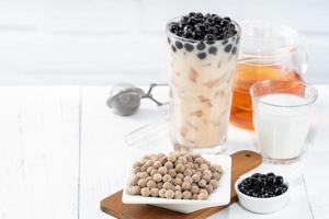 Bubble milk tea with tapioca pearl topping ingredient, famous Taiwanese drink on white wooden table background in drinking glass, close up, copy space photo