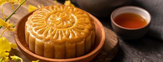 Mooncake, Moon cake for Mid-Autumn Festival, concept of traditional festive food on black slate table with tea and yellow flower, close up, copy space. photo