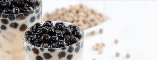 Bubble milk tea with tapioca pearl topping ingredient, famous Taiwanese drink on white wooden table background in drinking glass, close up, copy space photo