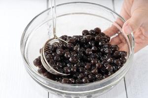 Making bubble tea, scoop and pour cooked brown sugar flavor tapioca pearl bubble balls into cup on white wooden table background, close up, copy space. photo