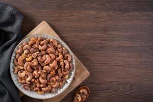 Cashew nuts with peel in a plate on wooden tray and table background, healthy raw food plate. photo