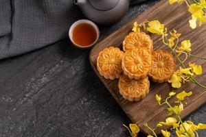 Mooncake, Moon cake for Mid-Autumn Festival, concept of traditional festive food on black slate table with tea and yellow flower, close up, copy space. photo