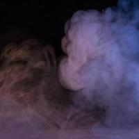 Conceptual image of multi-colored smoke isolated on dark black background and wooden table. photo