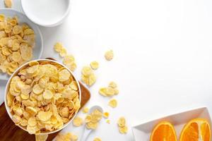 Corn flakes bowl sweeties with milk and orange on white background, top view, flat lay overhead layout, fresh and healthy breakfast design concept. photo