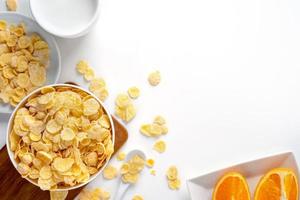 dulces de copos de maíz con leche y naranja sobre fondo blanco, vista superior, diseño plano superior, concepto de diseño de desayuno fresco y saludable. foto