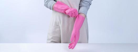 una joven ama de llaves en delantal lleva guantes rosas para limpiar la mesa, concepto de prevención de infecciones por virus, servicio de limpieza, cierre. foto