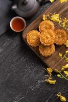 Mooncake, Moon cake for Mid-Autumn Festival, concept of traditional festive food on black slate table with tea and yellow flower, close up, copy space. photo