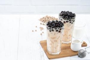 Bubble milk tea with tapioca pearl topping ingredient, famous Taiwanese drink on white wooden table background in drinking glass, close up, copy space photo