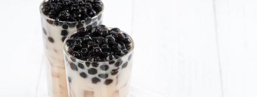 Bubble milk tea with tapioca pearl topping, famous Taiwanese drink on white wooden table background in drinking glass, close up, copy space photo