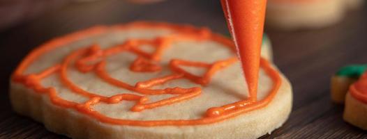 cerca de decorar lindas galletas de calabaza de halloween con glaseado en bolsa de hielo. foto