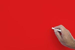 Male hand writes in white chalk pencil on a red background. Copy space. photo