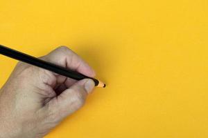 Male hand writes in black pencil on a yellow background. Copy space. photo