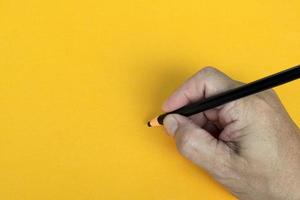 Male hand writes in black pencil on a yellow background. Copy space. photo