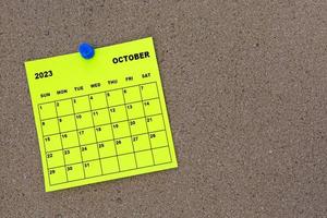 October 2023 yellow sticky note calendar with pin on cork bulletin billboard. photo