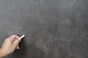 Male hand writes in white chalk pencil on a chalkboard background. Copy space. photo