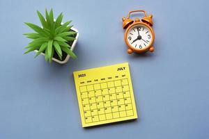 July 2023 calendar on adhesive note with alarm clock set at 8 o'clock. photo