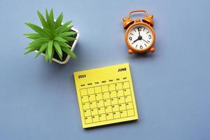 June 2023 calendar on adhesive note with alarm clock set at 8 o'clock. photo