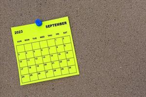 September 2023 yellow sticky note calendar with pin on cork bulletin billboard. photo