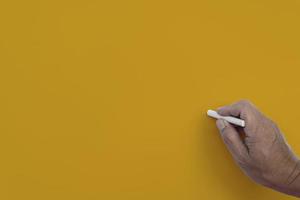 Male hand writes in white chalk pencil on a yellow background. Copy space. Teaching concept.Male hand writes in white chalk pencil on a yellow background. Copy space. photo