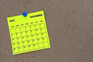 November 2023 yellow sticky note calendar with pin on cork bulletin billboard. photo