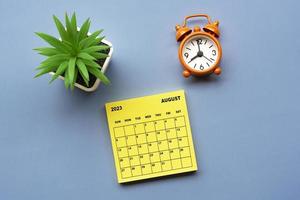 August 2023 calendar on adhesive note with alarm clock set at 8 o'clock. photo