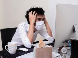 joven asiático con mascarilla trabajando en una computadora portátil durante la pandemia del coronavirus foto