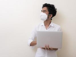 Business man in medical face mask works on laptop at home photo