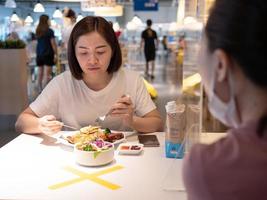 Asian woman sitting separated in restaurant eating food with table shield plastic partition to protect infection from coronavirus covid-19 photo