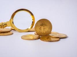 réplica de bitcoin dorado y lupa sobre fondo blanco.concepto de negocios y finanzas. foto