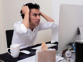 Serious Asian man is working with laptop in his apartment bedroom in concept of Work From Home and Work at Home photo