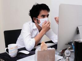 joven asiático con mascarilla trabajando en una computadora portátil durante la pandemia del coronavirus foto