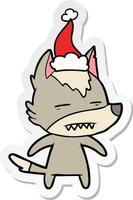 sticker cartoon of a wolf showing teeth wearing santa hat vector