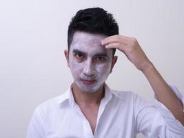 Asian handsome young man applying cream at his face with smiley face, Skin care concept photo