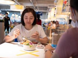 Asian woman sitting separated in restaurant eating food with table shield plastic partition to protect infection from coronavirus covid-19 photo