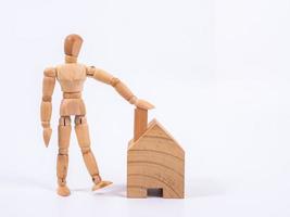 Man leaned against the model of a house isolated on white background. Concept with a wooden puppet photo