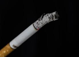 Cigarrillo encendido con humo sobre fondo negro foto