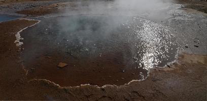 Steaming geyser in Iceland with mineral deposits around it photo