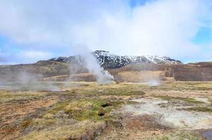 Steaming geysir with ice top mountains in the landscape photo