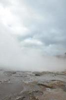 Blue sky breaking out of the clouds with a steaming geyser photo