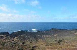 aguas azules del océano frente a una costa de roca de lava foto