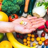 Hand holding food supplements over vegetables and fruits for a healty lifestyle photo