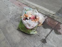 bolsas de basura de residuos de alimentos de plástico en la calle del pavimento. maloliente a podrido, insalubre para las vías respiratorias. foto